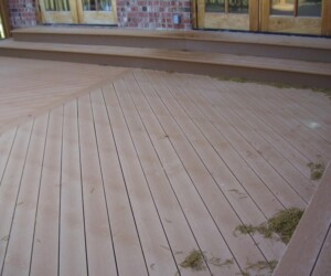 A wooden deck with built-in bench seating and debris scattered on the surface, set against brick and glass doors.