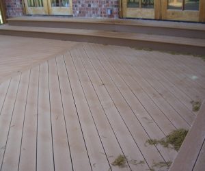 A wooden deck with built-in bench seating and debris scattered on the surface, set against brick and glass doors.