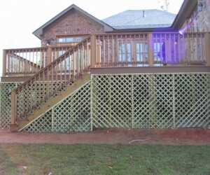 A wooden deck with railing on the side of a brick house, featuring lattice skirting and a staircase leading to the ground.
