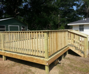 A newly built wooden deck with railings and stairs in the backyard of a house, featuring a green shed and trees in the background.