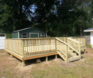 A newly constructed wooden deck with railings and stairs in a backyard, next to a green shed and surrounded by trees.
